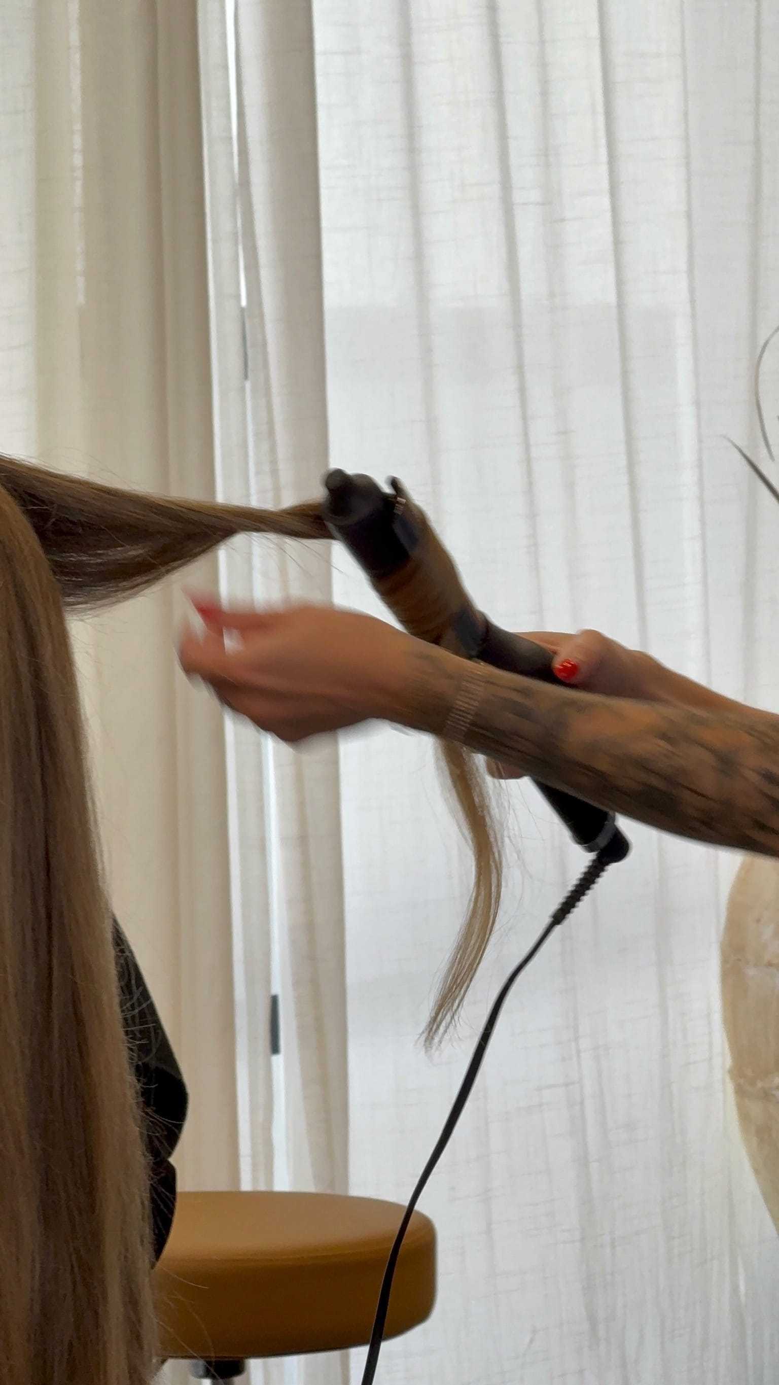 Hairdresser curling brown hair with a styling wand in a salon setting.