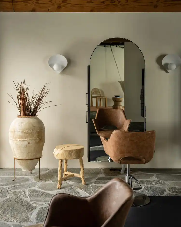 Cozy salon with brown leather chair, large vase, wooden stools, and arched mirror.