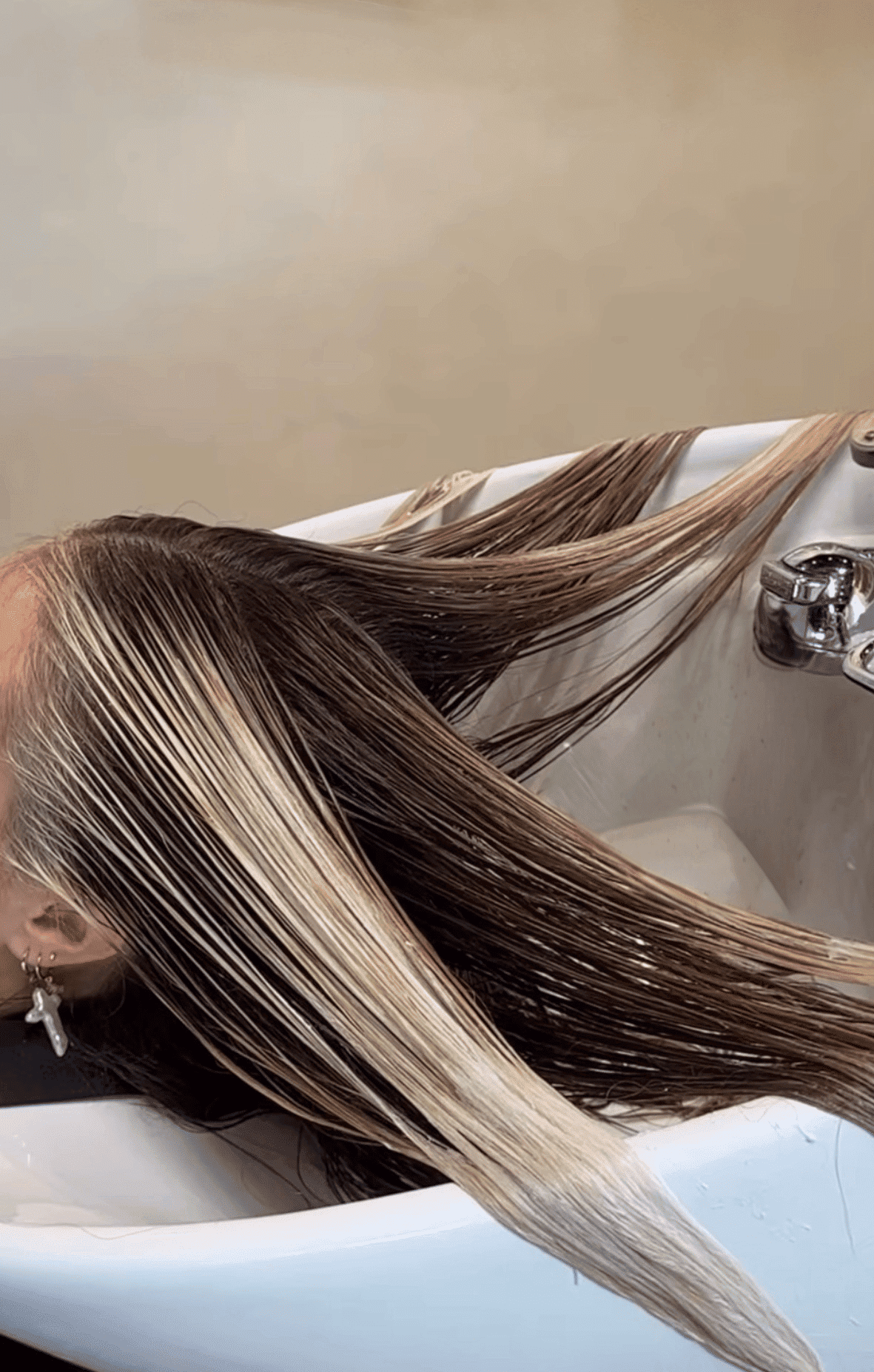 Person getting hair washed at a salon sink, showing wet, highlighted long hair.