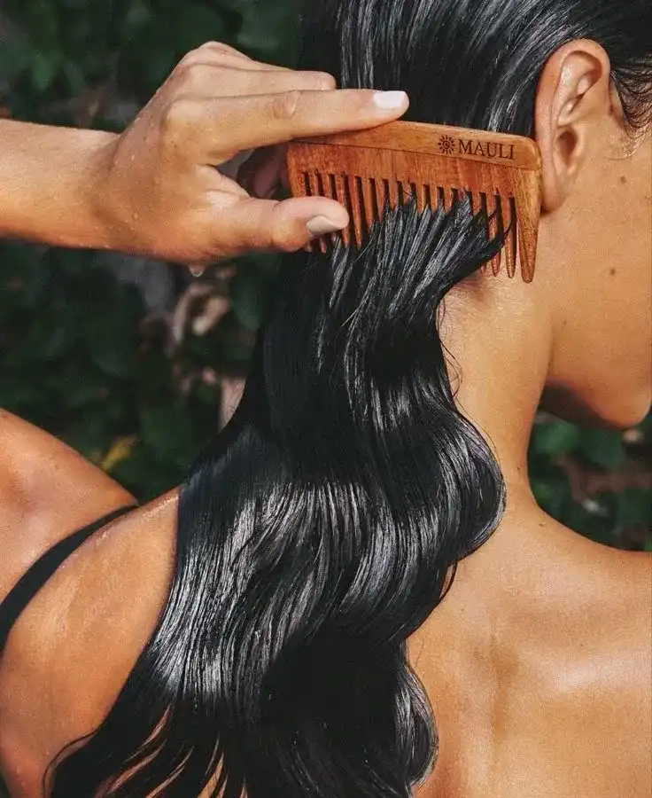 Wooden comb used to straighten long, wet, black hair outdoors.
